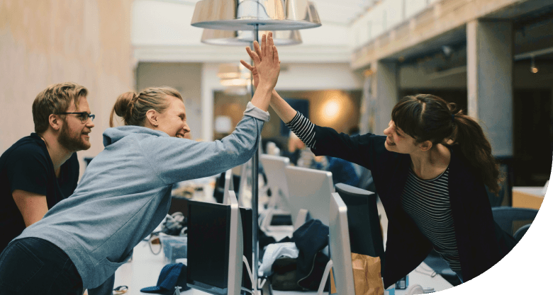 Workers in an office setting reaching across their workstations giving hi-fives to one another